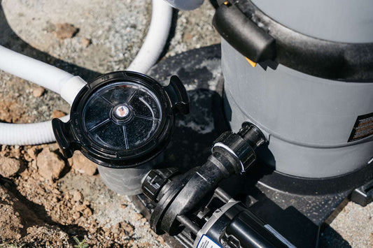 Close-up of a My Store Waterway Cartridge Filter, shown with gray and black glass-filled polymer construction and attached pipes, set on a concrete pad near dirt and rocks. The clear pump lid and visible connections are highlighted.
