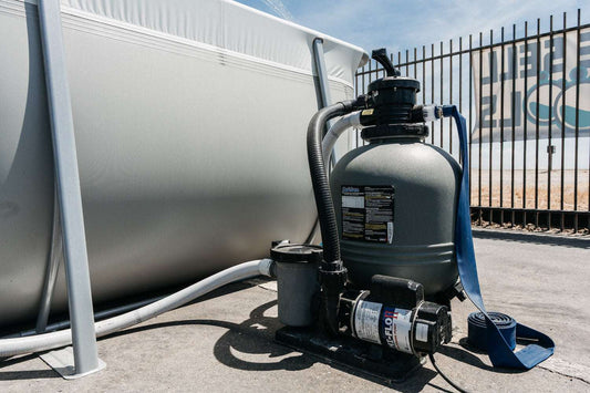 A My Store Waterway Sand Filter with hoses is connected to a Kona Above Ground Pool outdoors near a metal fence on a sunny day.