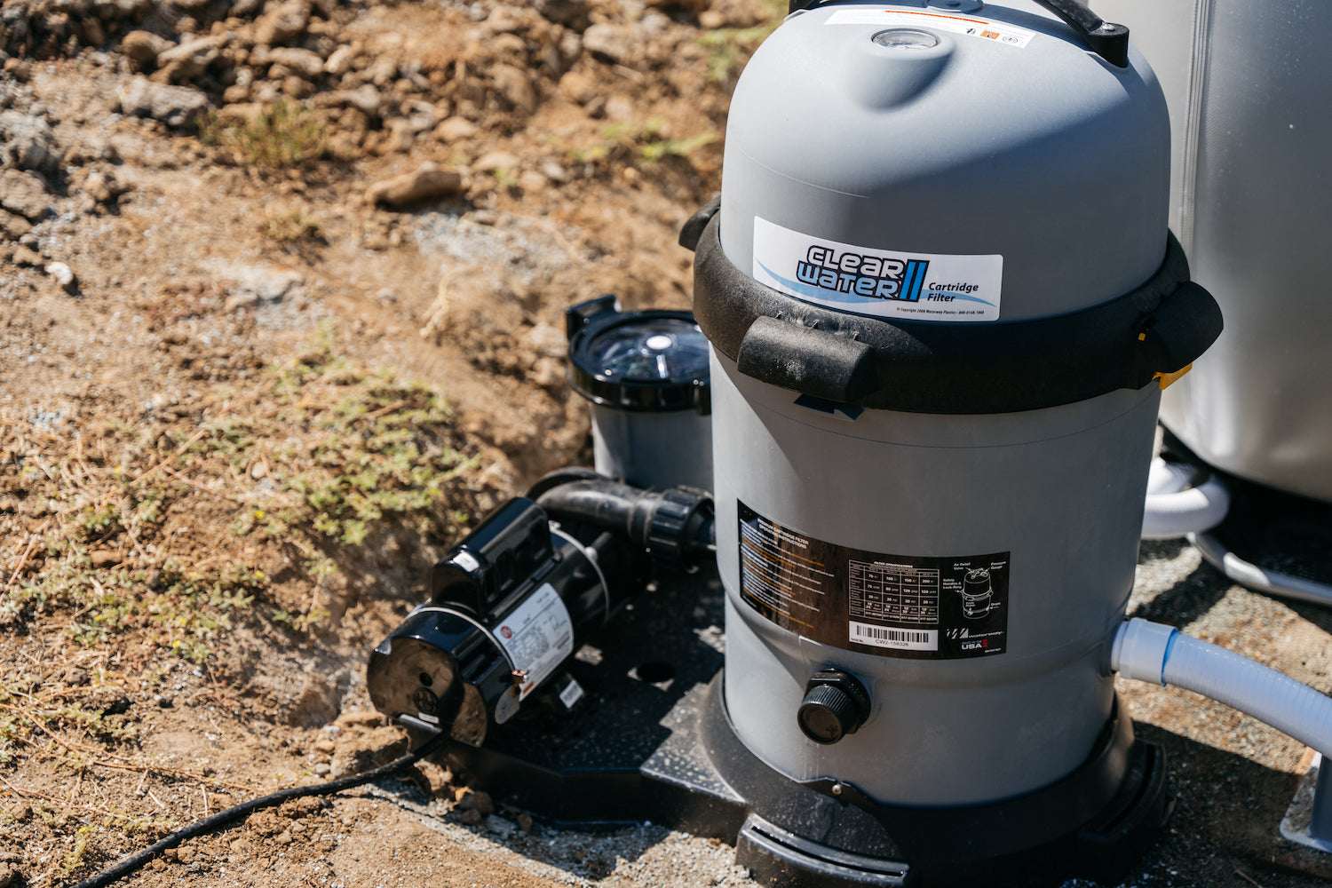 A close-up of a gray My Store Waterway Cartridge Filter with durable glass-filled polymer construction, black pump, and white piping, set on dirt and gravel outdoors.